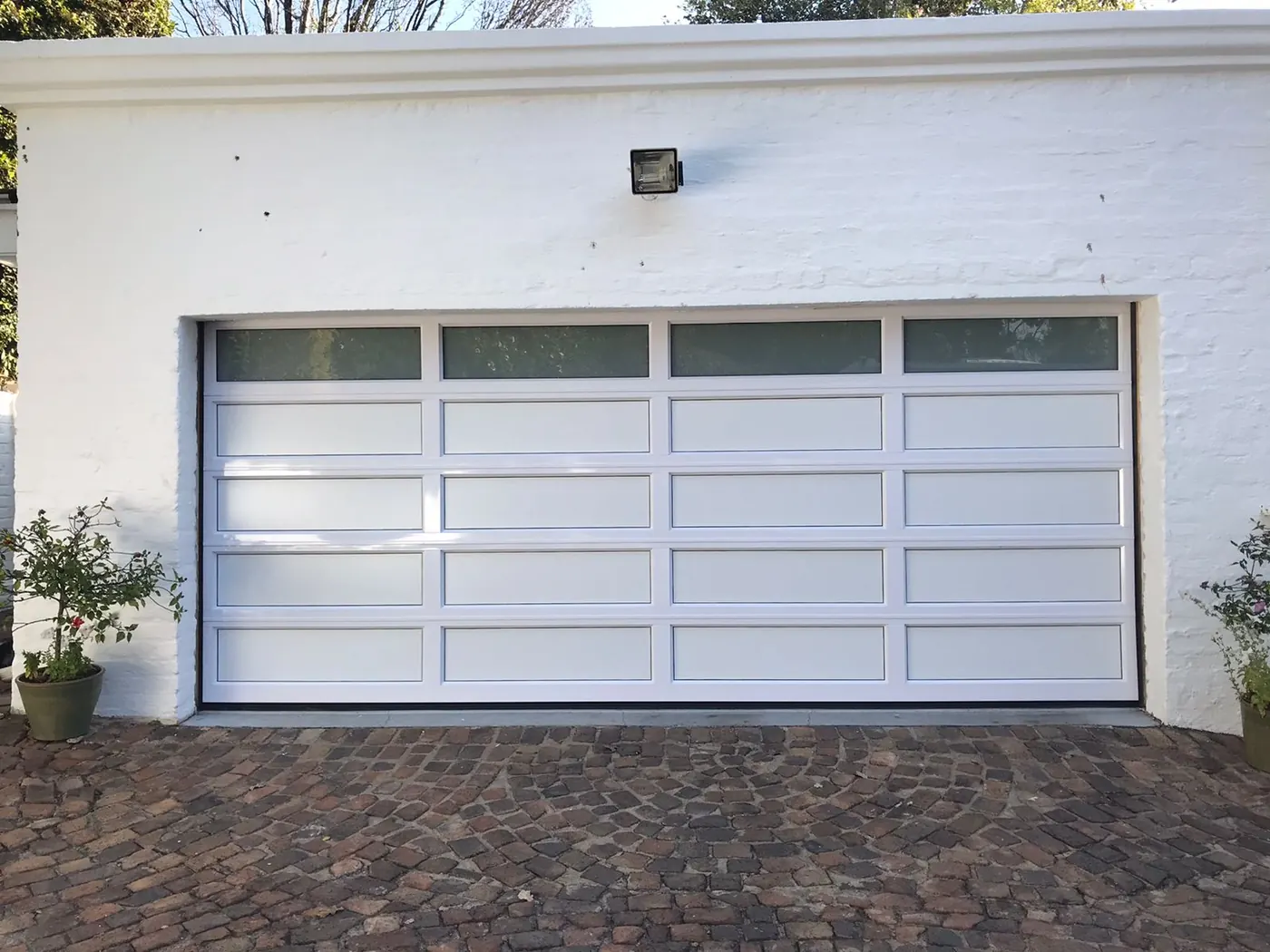 Modern white aluminium garage door with framed panels and upper glazed sections