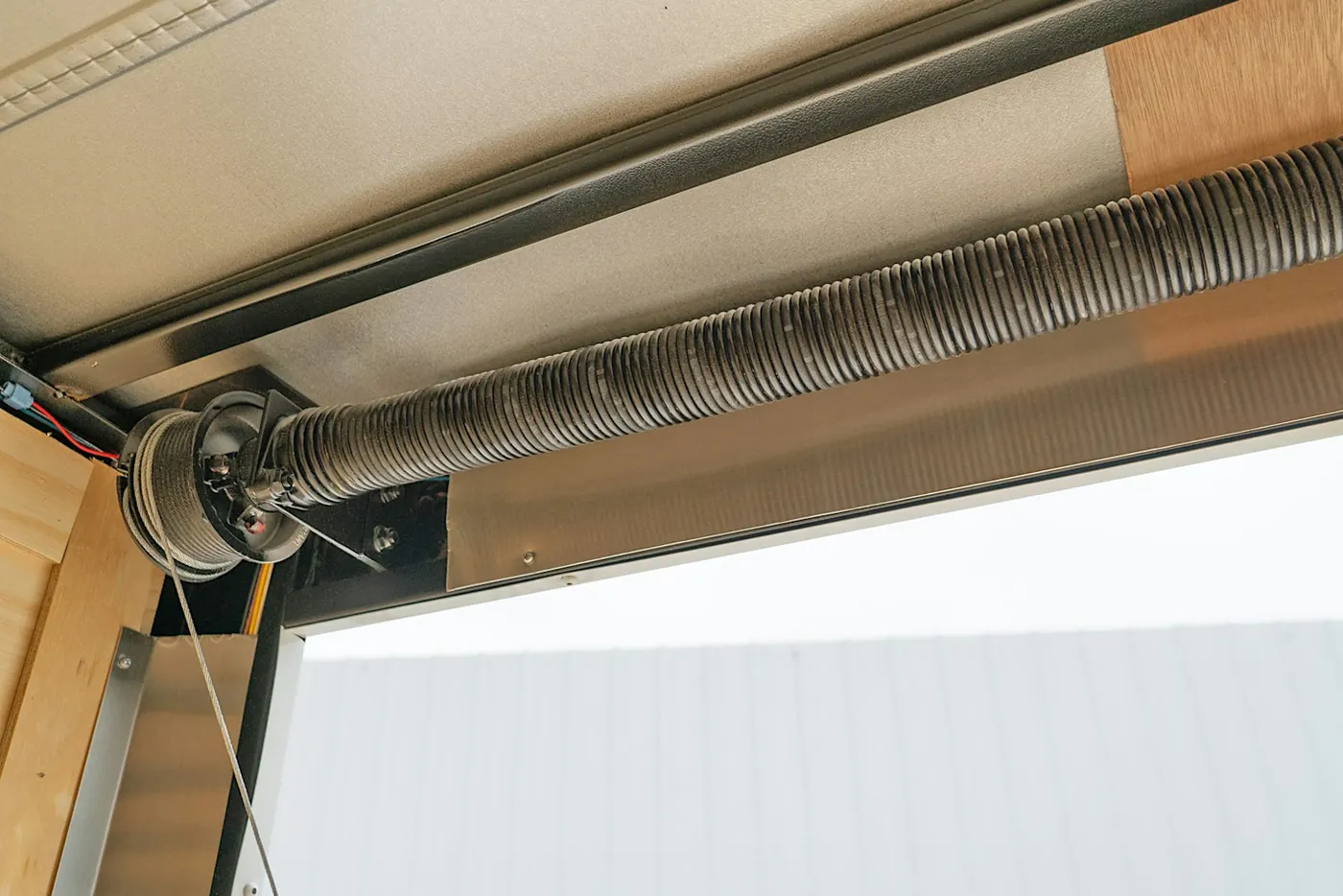 Installed garage door torsion spring, cable drum and lifting cable above the door opening